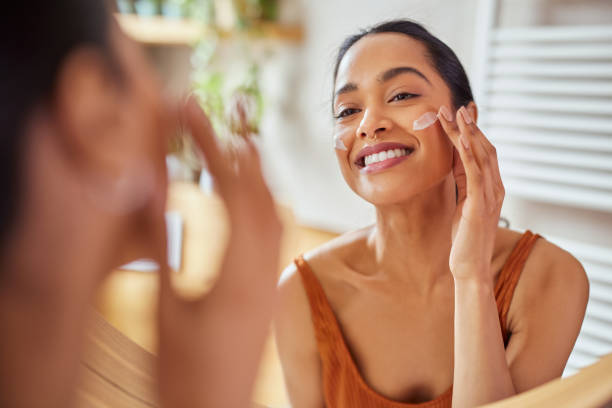 Smiling woman applying facial cream while looking in mirror