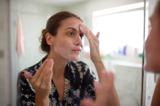 Woman applying facial cream while looking in mirror