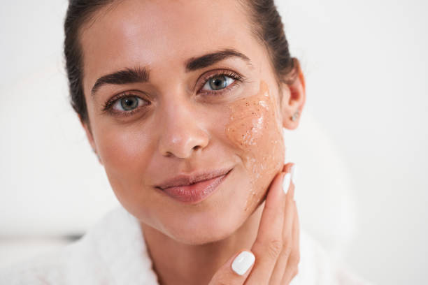 Close-up portrait of a woman with a facial scrub on her cheek, smiling at the camera