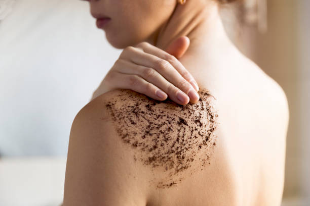 Woman applying a coffee scrub on her shoulder in a spa treatment session