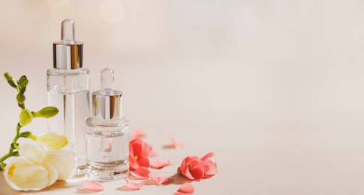 Glass skincare serum bottles with droppers and fresh flowers on a soft beige background